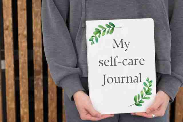 woman in a gray sweatshirt holding a self-care journal