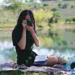 woman sitting in a park on a picnic blanket taking pictures