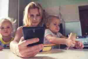 mother focused on her phone while holding her kids