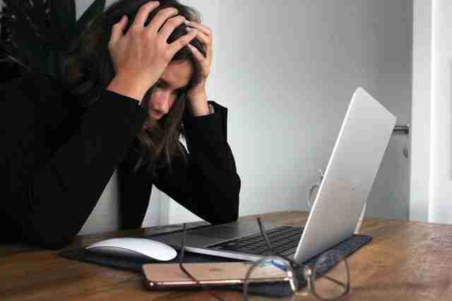 woman with her hand on her head looking at her computer and feeling anxiety