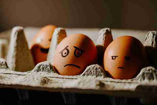 carton of brown eggs with faces showing emotions drawn on them