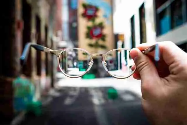 a hand holding a pair of glasses that brings a portion of the street into focus.