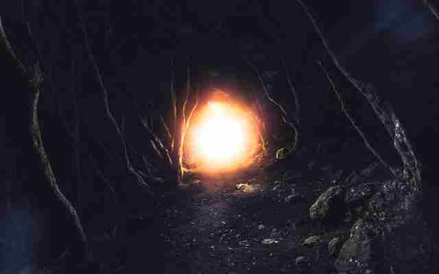 Foreboding looking cave with tree roots  a light shines from the cave emanating a sense of anger