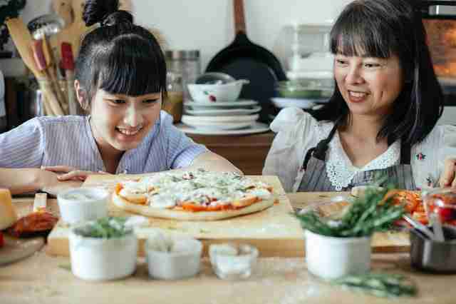 woman helping preteen learn to cook and watching with a smile