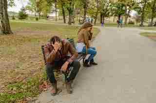 a couple in the park sitting on a bench facing away from each other with their heads in their hands because of marital problems