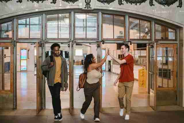 three friends that are good people giving each other a high five as they walk out of a building together