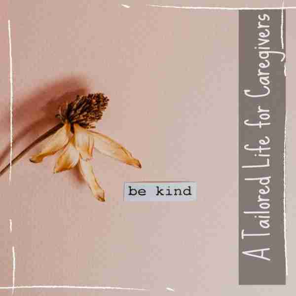 dried flower on a pink background next to a slip of paper with the words be kind